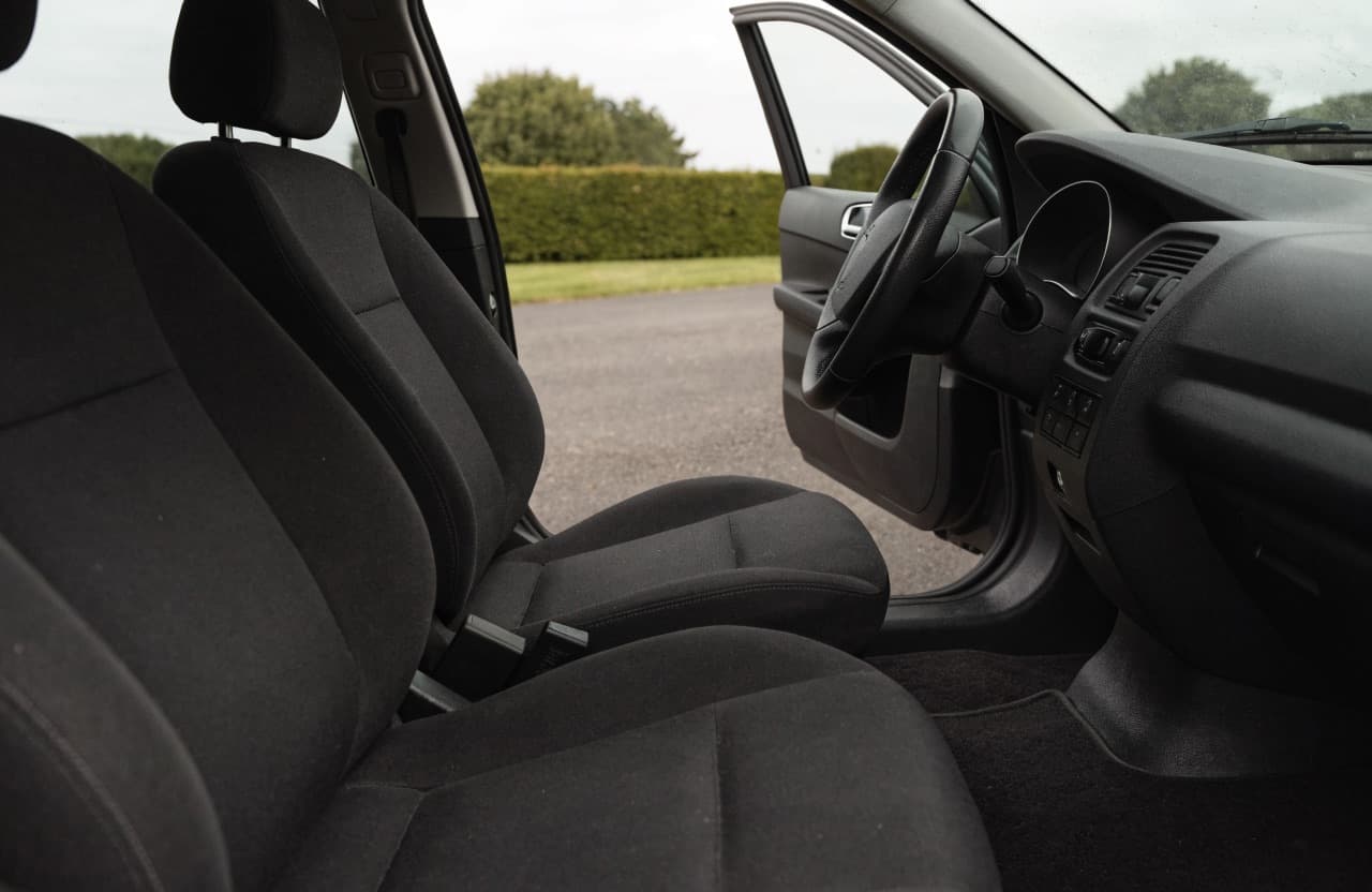 Het gereinigde interieur van een middenklasse auto gezien door de geopende bestuurdersdeur: gestofzuigde stoelen, stofvrij dashboard en rechtliggende matten.