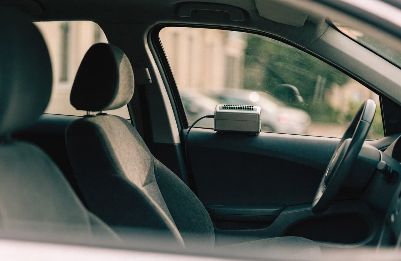 Een ozongenerator staat op de bestuurdersstoel van een leeg auto-interieur, met de stroomkabel door een kier van het raam naar buiten.