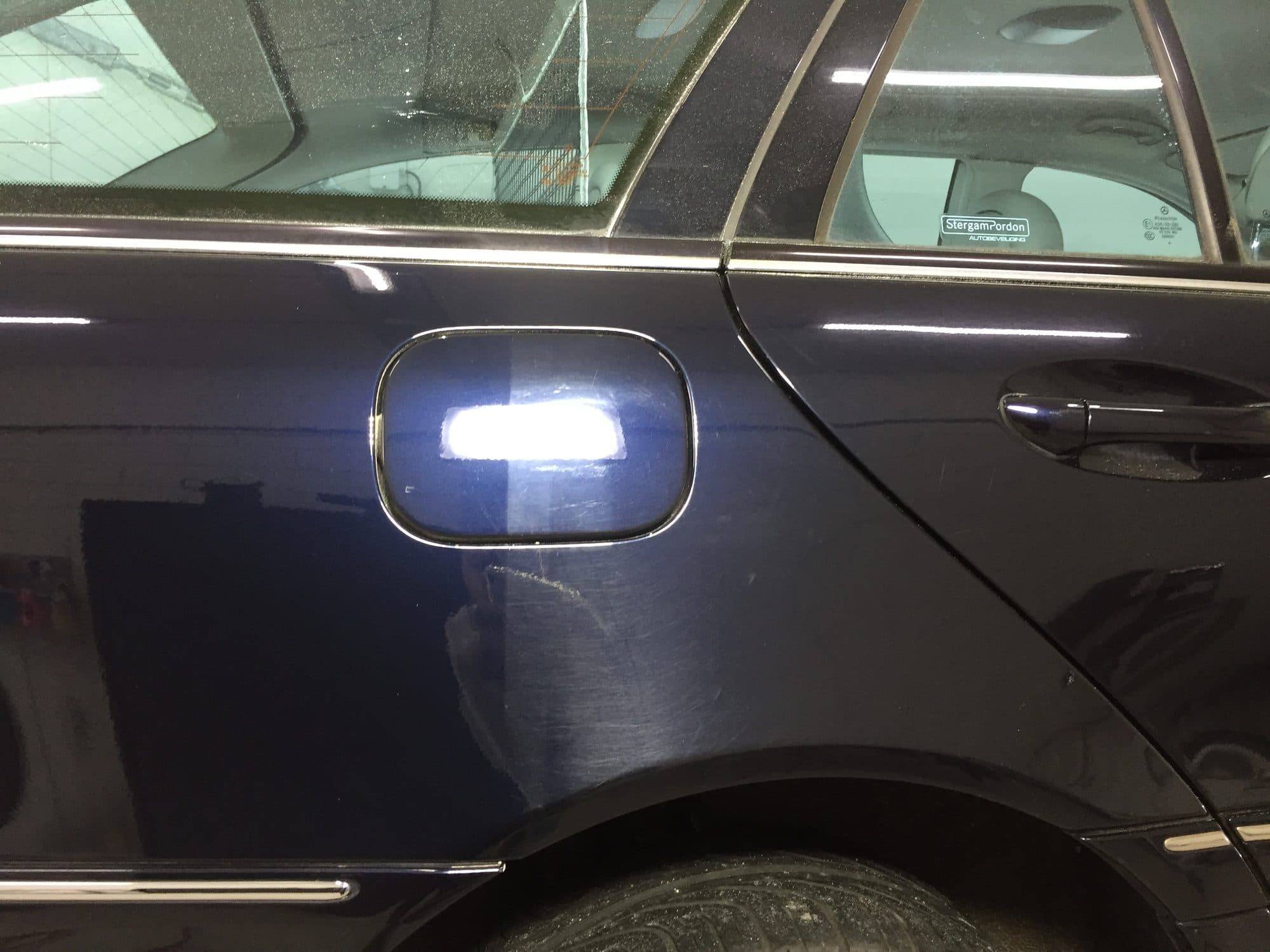 Donkerblauw autopaneel in de werkplaats waarop het verschil tussen het gepolijste en het niet-gepolijste deel zichtbaar is onder werklamp.